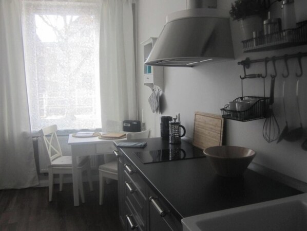 Una cocina con estufa, un lavabo, una ventana con cortinas y una silla.