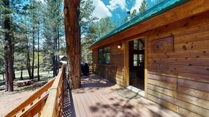 A wooden cabin with a deck, surrounded by trees.