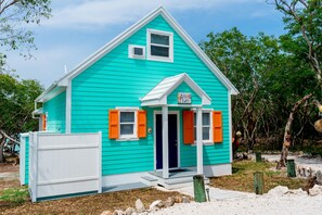 A turquoise house with a white door and orange shutters, surrounded by trees and a white fence. - Anchor's Away, Russell Island (Russell Island)
