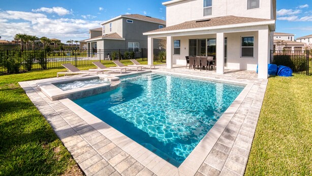 A swimming pool with a patio area, a covered seating area, and a two-story house in the background. - Charming Disney Vacation House - The Best Clubhouse (Kissimmee)