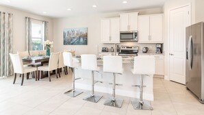 A modern kitchen with white cabinets, stainless steel appliances, and a central island with bar stools. - Charming Disney Vacation House - The Best Clubhouse (Kissimmee)