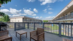 A deck with wooden furniture, a barbecue grill, and a view of a building with balconies. - Dutchland Motel (Lancaster)