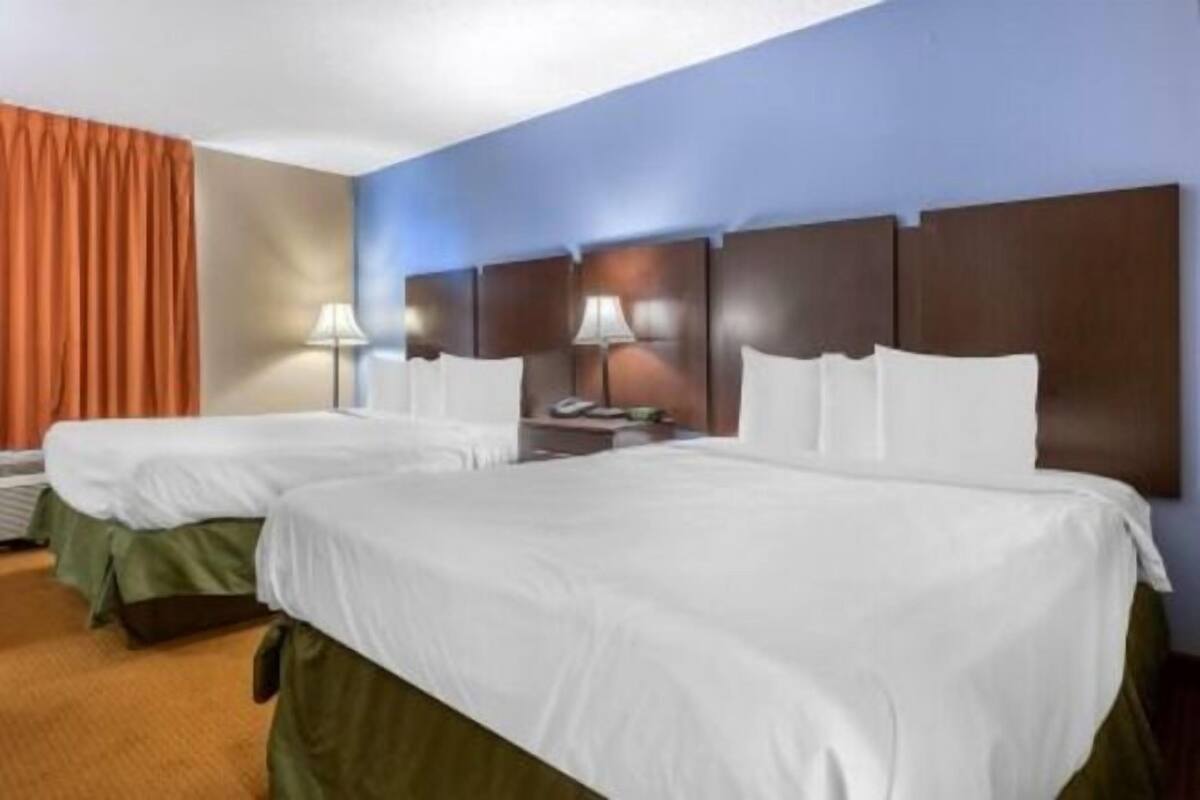 Une chambre d’hôtel avec deux lits, une table de chevet, une lampe et une fenêtre avec des rideaux.