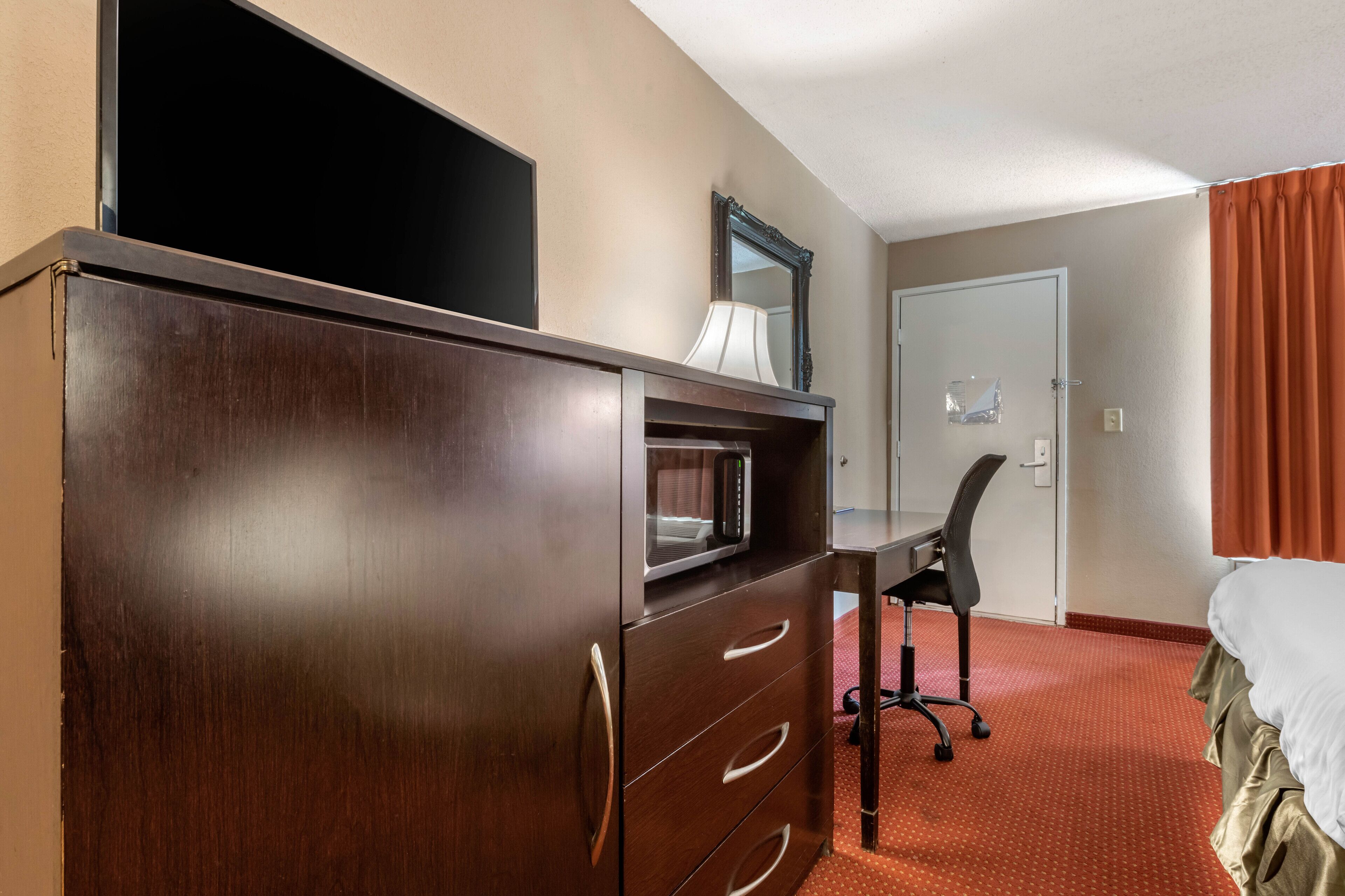 Une chambre d’hôtel avec une commode en bois, un bureau avec une lampe, une chaise et un lit.