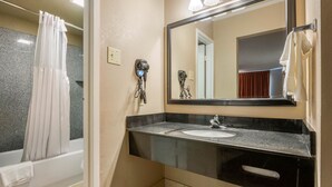 A bathroom with a bathtub, a sink, a mirror, and two hair dryers.