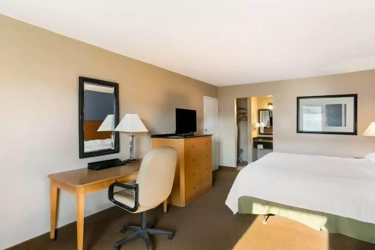 Une chambre d’hôtel comprenant un lit, un bureau avec une chaise, une télévision et une commode.