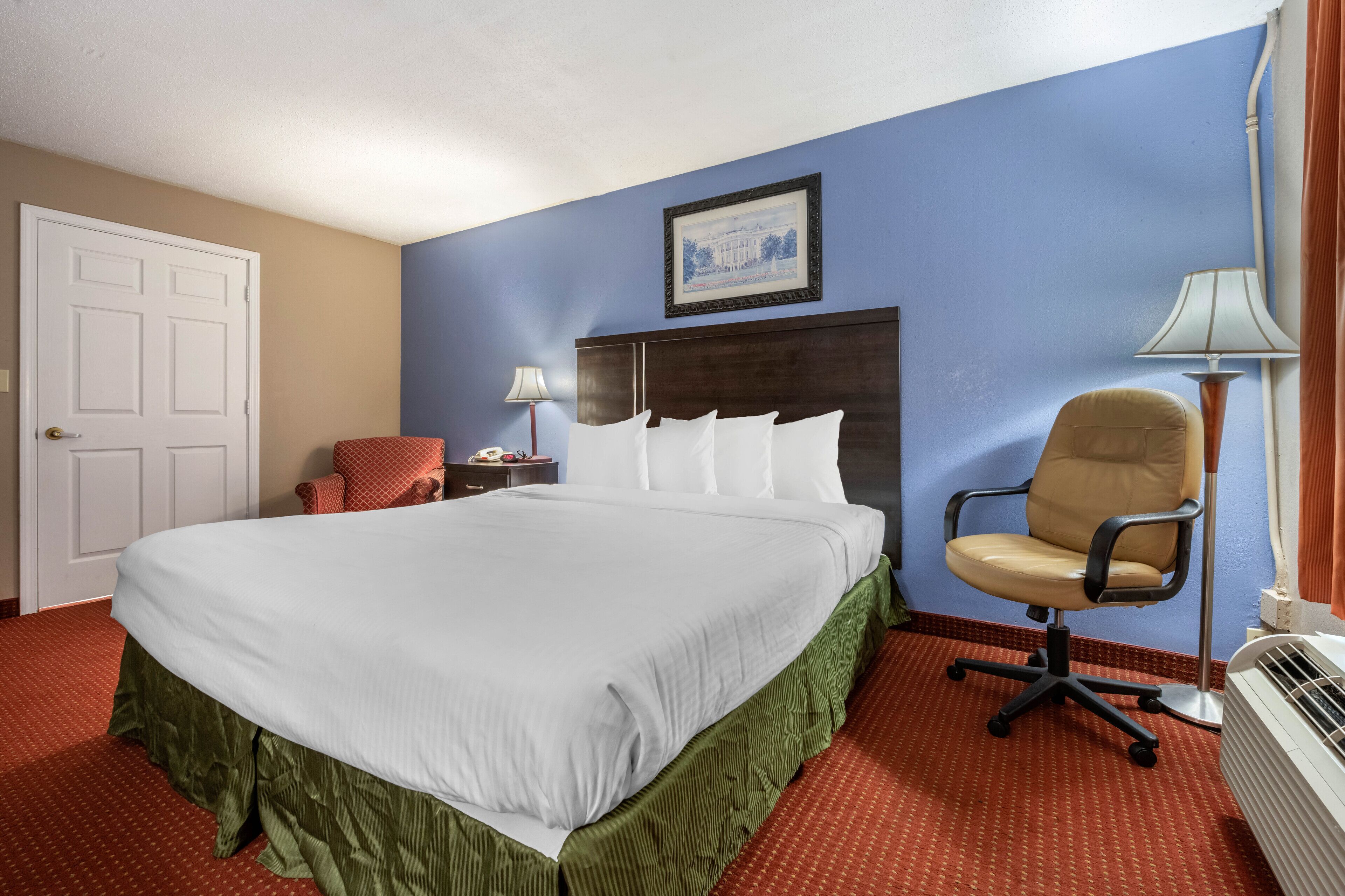 Quarto de hotel com uma cama grande, uma cadeira, uma escrivaninha e uma luminária.