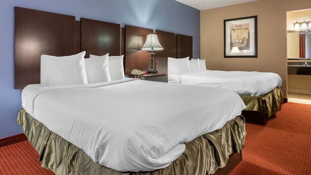 A hotel room with two beds, a nightstand with a lamp, a framed picture on the wall, and a bathroom mirror. - Dutchland Motel (Lancaster)