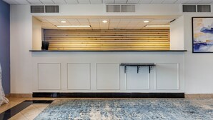 A reception area with a wooden reception desk, a black and white tiled floor, and a blue and white patterned rug. - Dutchland Motel (Lancaster)