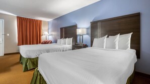 A hotel room with two beds, a nightstand, a lamp, and a window with curtains.