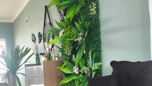 A modern living room with a black sofa, a green wall decorated with plants, and a wooden cabinet.
