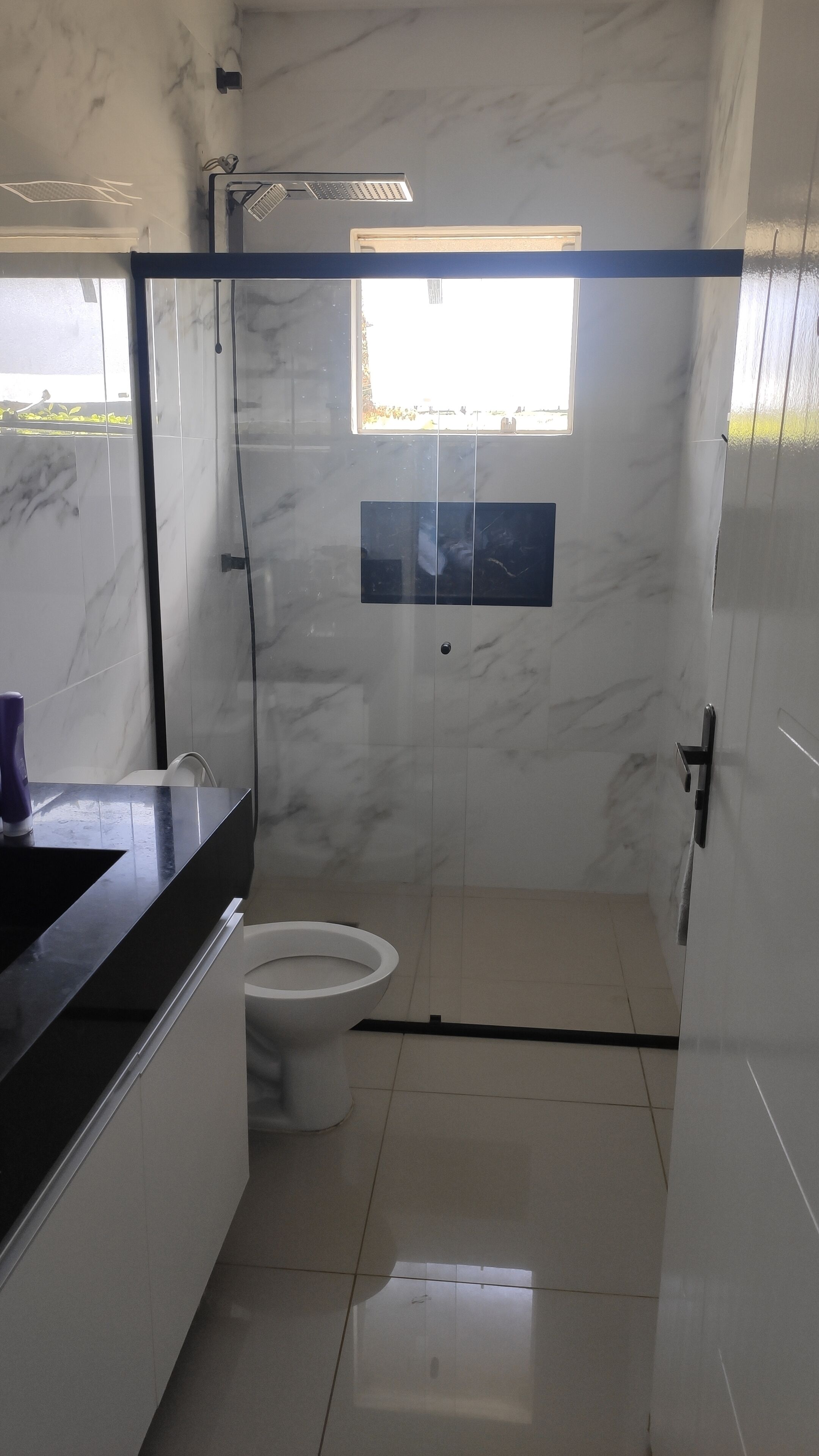 A modern bathroom with a glass shower enclosure, a toilet, and a sink with a marble countertop.