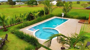 A rectangular swimming pool with a clear blue center, surrounded by a well-maintained lawn and palm trees.