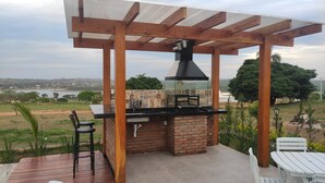 An outdoor barbecue area with a brick grill, wooden pergola, and seating.