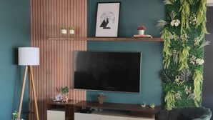 A modern living room with a flat-screen TV, dark green sofas, a coffee table, and a decorative plant wall.