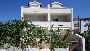 A two-story building with balconies, a stone wall in the foreground, and a clear blue sky. - Remarkable 2-bed Apartment in Srima With sea View (Vodice)