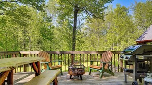 A wooden deck with picnic tables and chairs, a fire pit, and a grill. - Saranac Lake Cabin w/ Deck: Pets Welcome! (Saranac Lake)