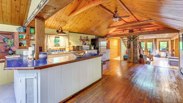 A spacious kitchen with wooden beams, a central island, and a stone fireplace. - Saranac Lake Cabin w/ Deck: Pets Welcome! (Saranac Lake)