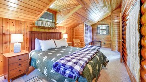 A cozy log cabin bedroom with a bed, nightstand, and a window with a view of the outdoors. - Saranac Lake Cabin w/ Deck: Pets Welcome! (Saranac Lake)