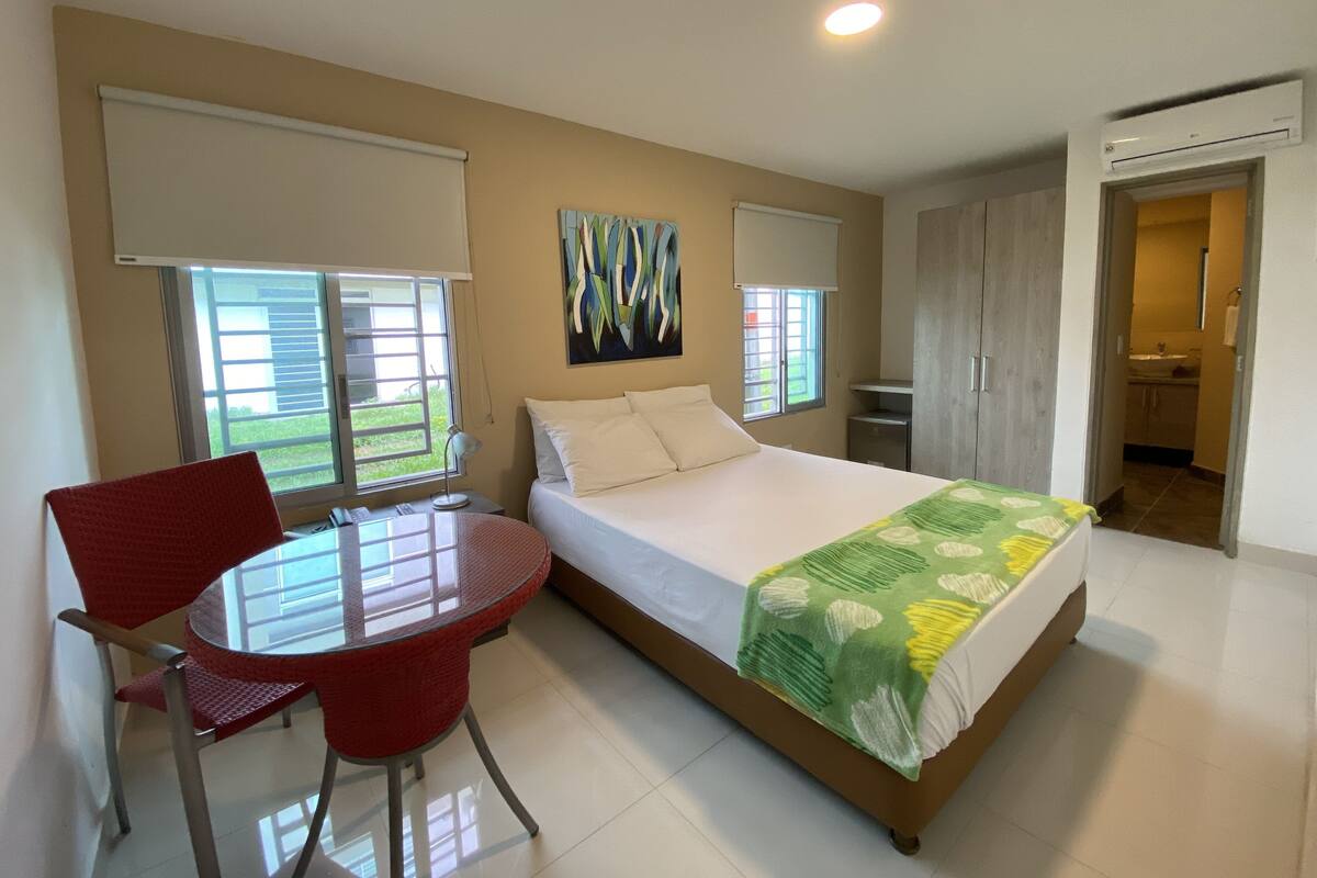 Une chambre à coucher comprenant un lit, un bureau avec une chaise, une fenêtre et un appareil de climatisation.