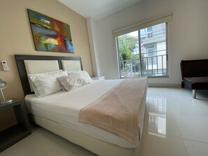 Une chambre d’hôtel moderne avec un grand lit, une table de chevet avec une lampe, un tableau au mur et une grande fenêtre donnant sur l’extérieur.