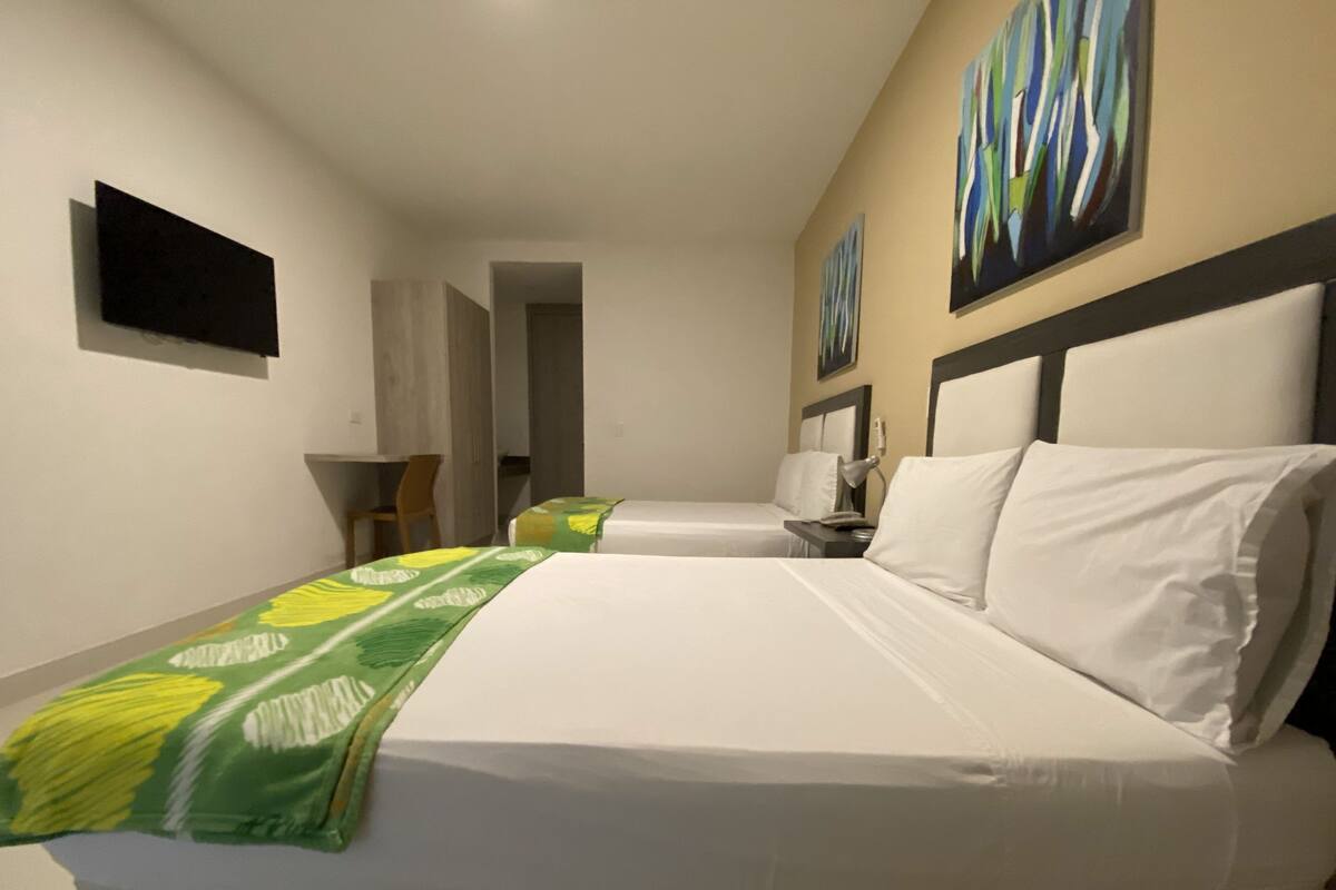 Une chambre d’hôtel avec deux lits, un bureau, une chaise et des œuvres d’art accrochées aux murs.