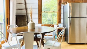 A dining area with a round table, white chairs, a wooden table, and a stainless steel refrigerator. - The Rocking A Frame - modern meets cozy. (Danbury)