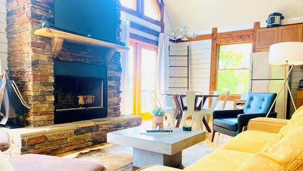A cozy living room with a stone fireplace, leather sofas, and a dining area with a table and chairs. - The Rocking A Frame - modern meets cozy. (Danbury)