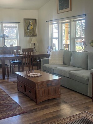 A living room with a wooden coffee table, a sofa, a dining table with chairs, and a painting on the wall.