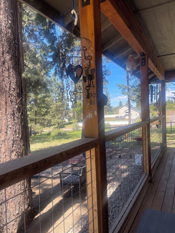 A wooden deck with a metal fence, a tree, and a view of a fenced area with a house in the background.
