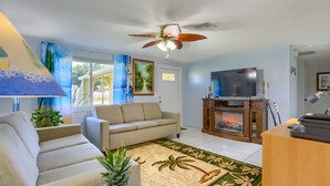 Ein Wohnzimmer mit einer Couch, einem Fernseher, einem Kamin und einem Deckenventilator.