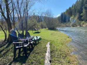A riverside picnic area with chairs and a swing set. - THE CABIN on Lake Creek River (Troy)