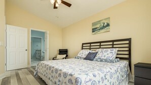 A bedroom with a bed, a nightstand, a ceiling fan, and a door leading to a bathroom. - Galveston Bay Views & Pier! San Leon Gulf Getaway (San Leon)