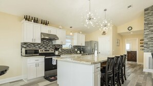 A spacious kitchen with white cabinetry, a large island, and a modern chandelier. - Galveston Bay Views & Pier! San Leon Gulf Getaway (San Leon)