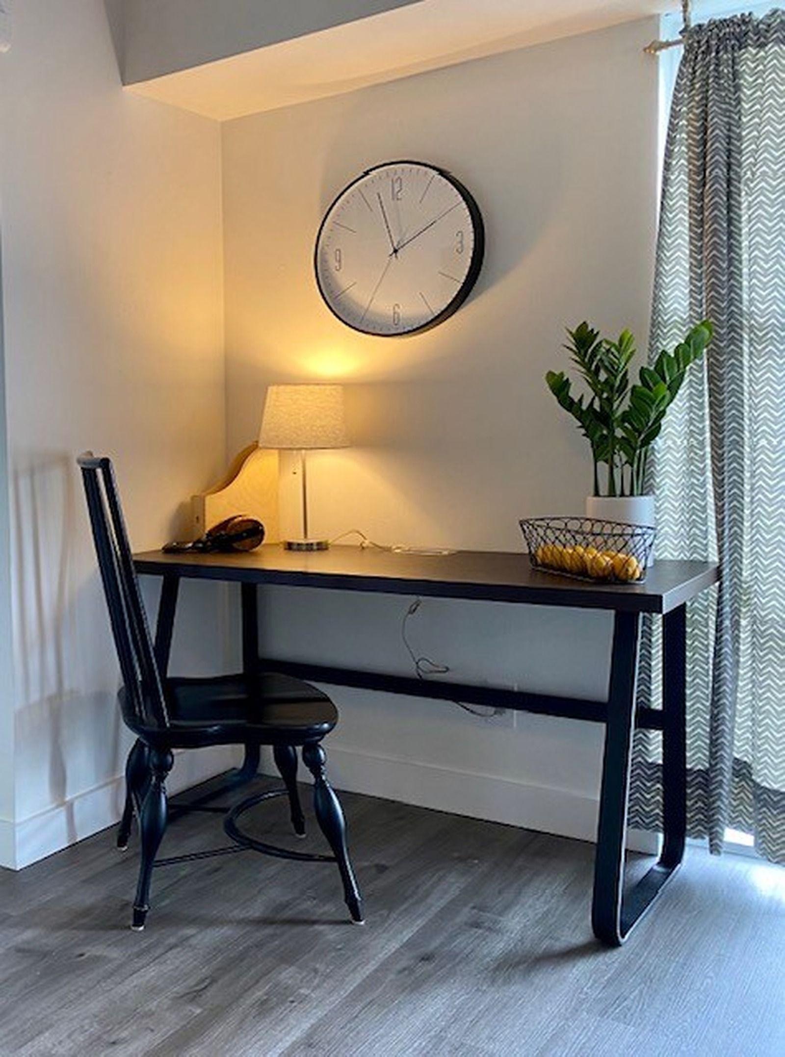 A desk with a chair, a wall clock, a lamp, and a potted plant.