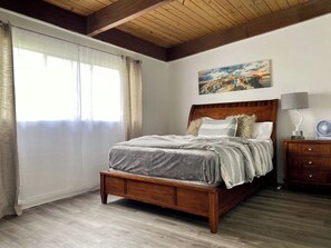 A bedroom with a wooden bed, a nightstand, a lamp, and a painting on the wall. - Cozy 3BR Retreat Near DC - Pool & Playground (Annandale)