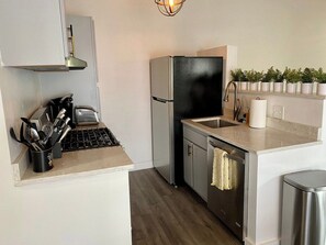 A compact kitchen with a refrigerator, sink, and a countertop with utensils. - Cozy 3BR Retreat Near DC - Pool & Playground (Annandale)