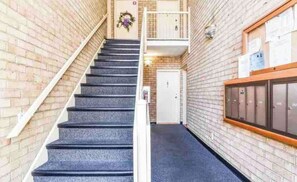 A staircase leading to a door with a wreath on the wall, a bulletin board with papers, and a row of lockers. - Cozy 3BR Retreat Near DC - Pool & Playground (Annandale)