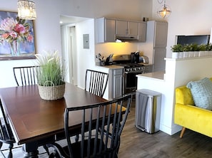 A modern kitchen with a dining area, a yellow sofa, and a painting on the wall. - Cozy 3BR Retreat Near DC - Pool & Playground (Annandale)