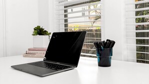Una computadora portátil sobre una mesa blanca, con una ventana al fondo.