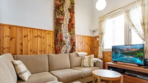 Una sala de estar acogedora con un panel de madera, un televisor de pantalla plana grande, un sofá y una pequeña mesa redonda con revistas.