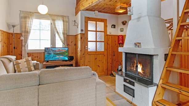 Una sala de estar acogedora con chimenea, techo de madera y televisor sobre un mueble de madera.