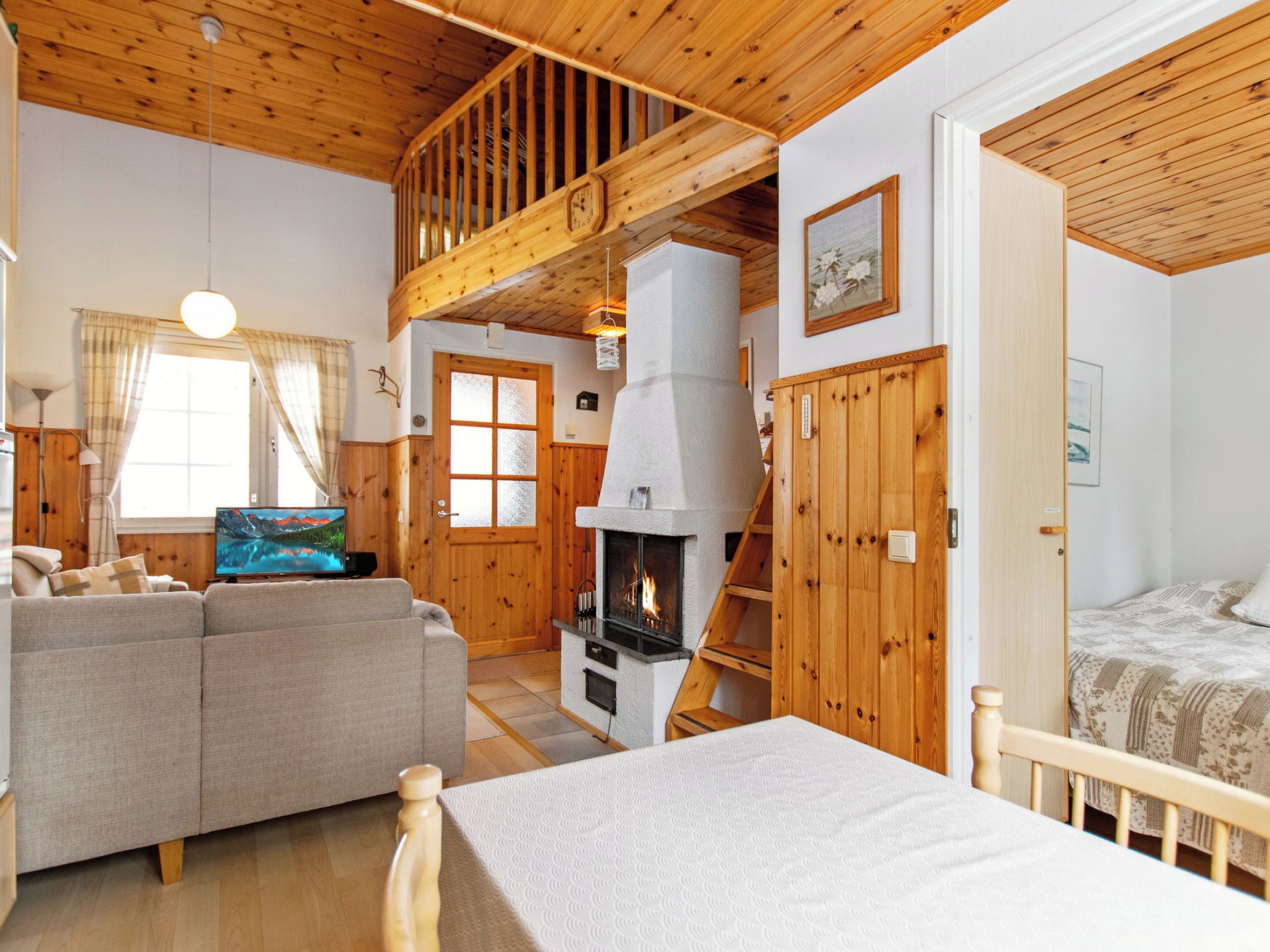 A cozy cabin interior with a fireplace, wooden walls, a sofa, and a bed.