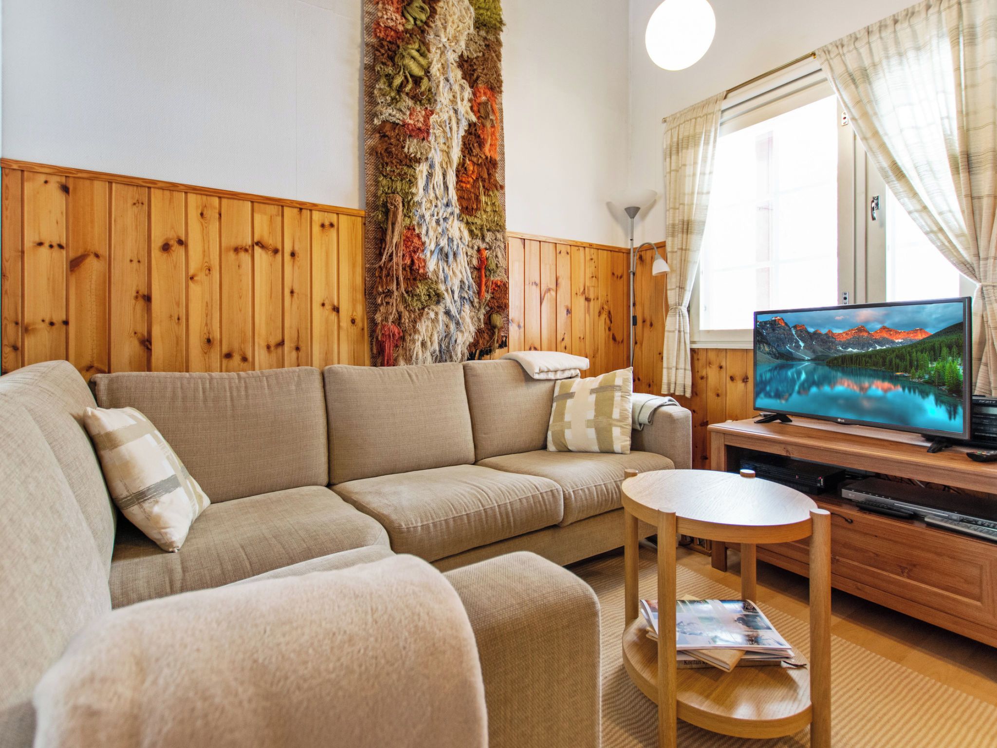 Una sala de estar con un sofá, una mesita de madera, un televisor y una pared decorada con un tapiz texturizado.
