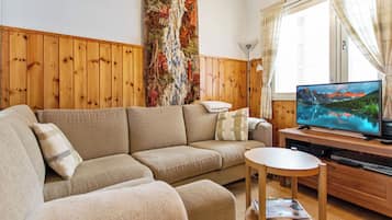 Una sala de estar con un sofá, una mesita de madera, un televisor y una pared decorada con un tapiz texturizado.