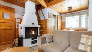 Interior acogedor de una cabaña con chimenea, paredes de madera, un sofá y una mesa de comedor.