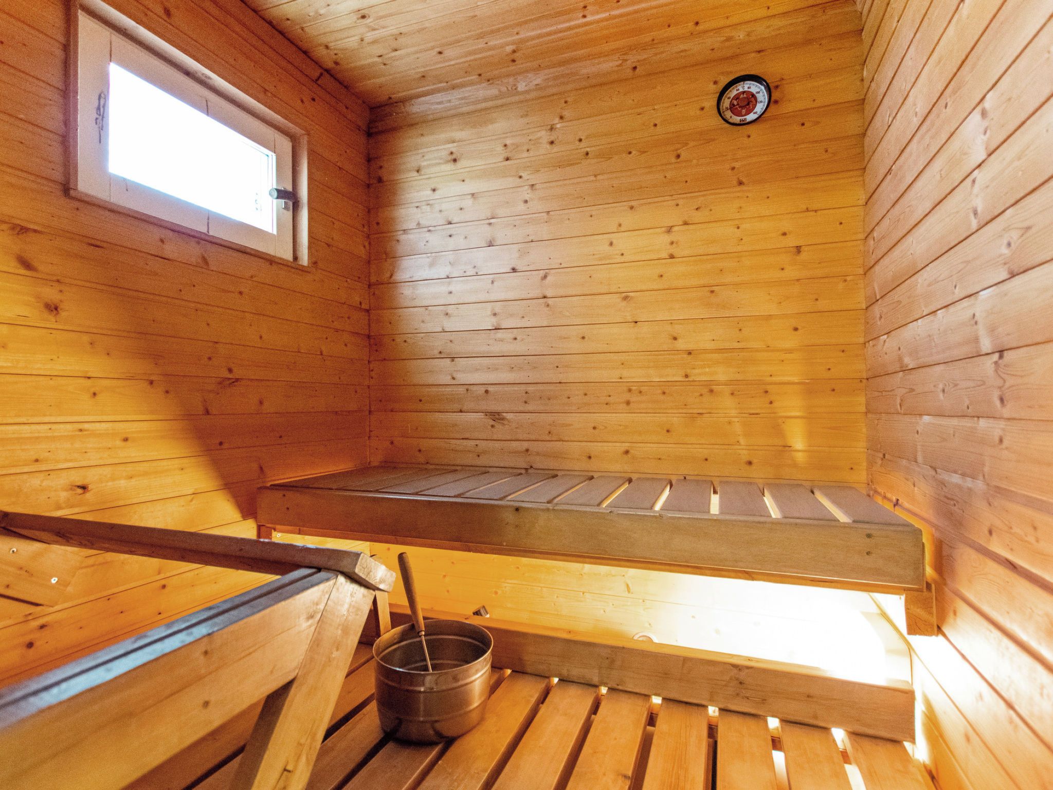 Un sauna avec des murs en bois, un banc, une fenêtre et un thermomètre fixé au mur.