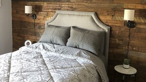 Camera da letto con pannello murale in legno, un letto con biancheria a motivi, due lampade da comodino e una ventola a soffitto.
