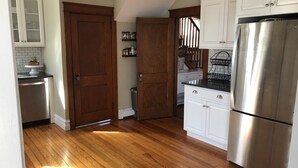 Cucina con pavimento in legno, mobili bianchi, frigorifero in acciaio inossidabile e lavastoviglie.
