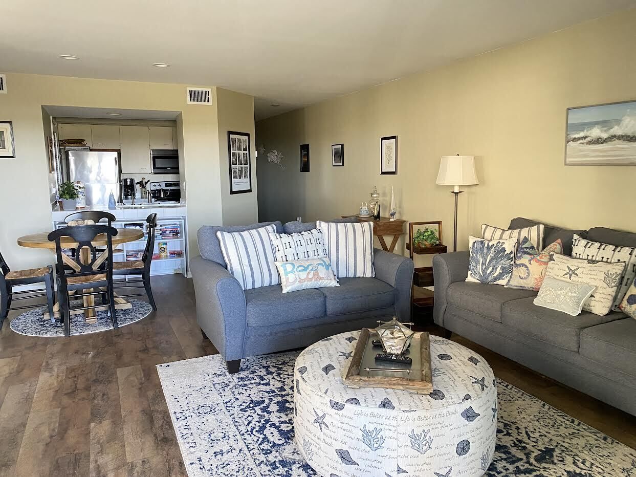 A living room with a grey sofa, a coffee table, and a dining area with a wooden table and chairs.